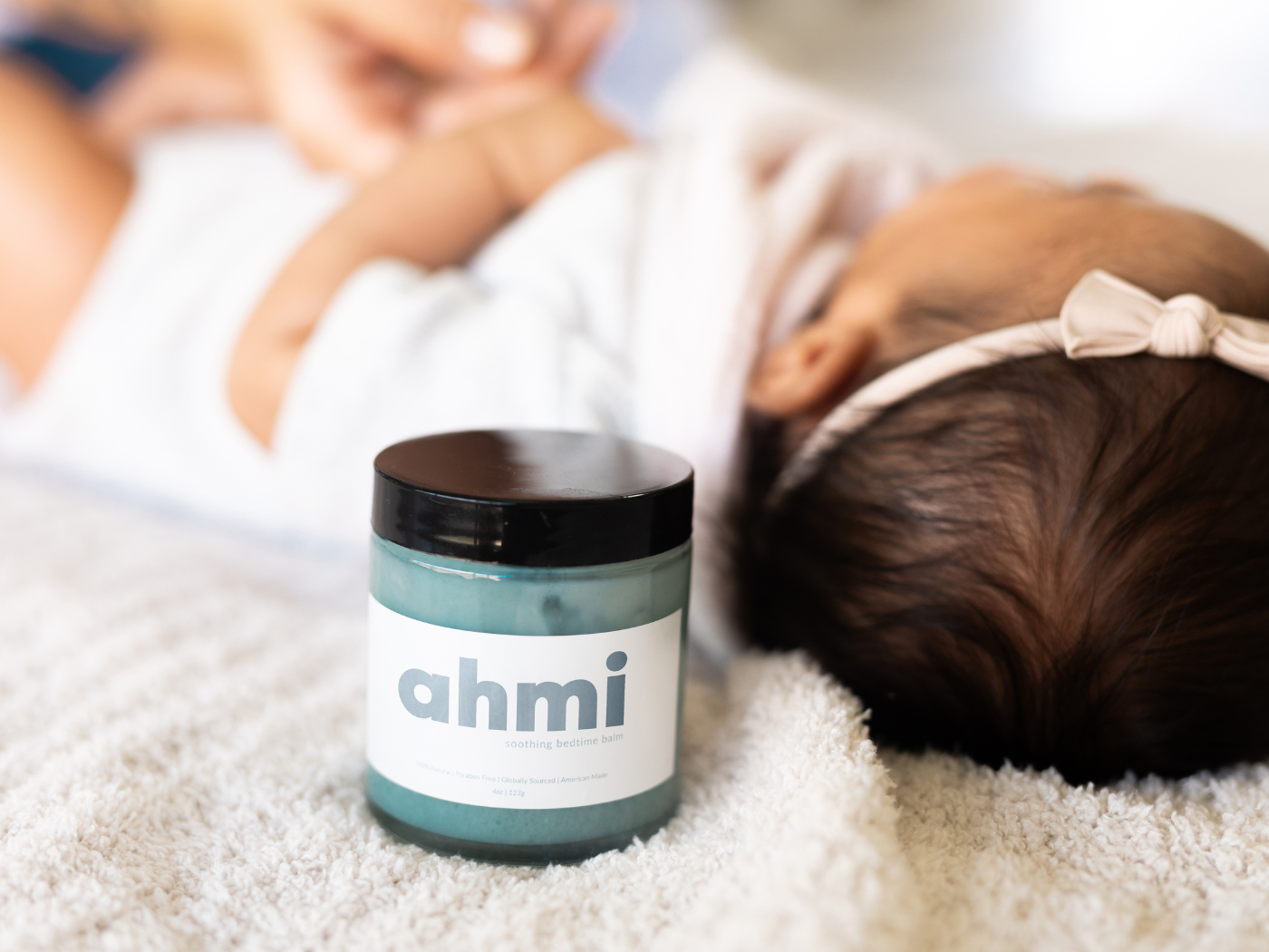 Jar of ahmi cream on a blanket with a baby in the background